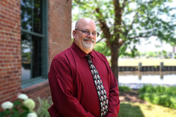 a man in a red shirt and tie standing in front of a brick building